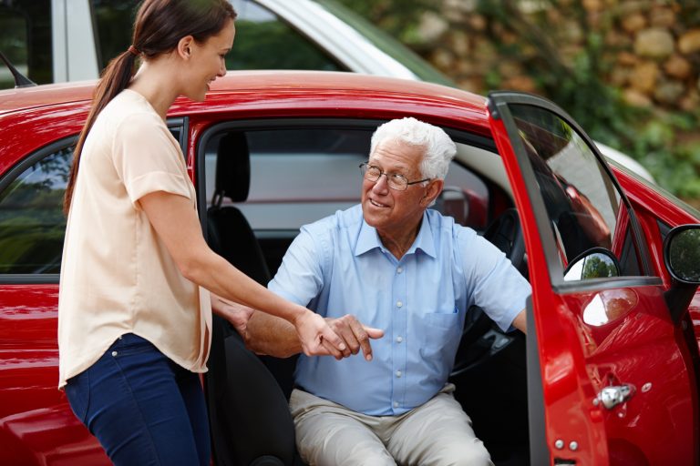 Woman helping her senior father out of the car