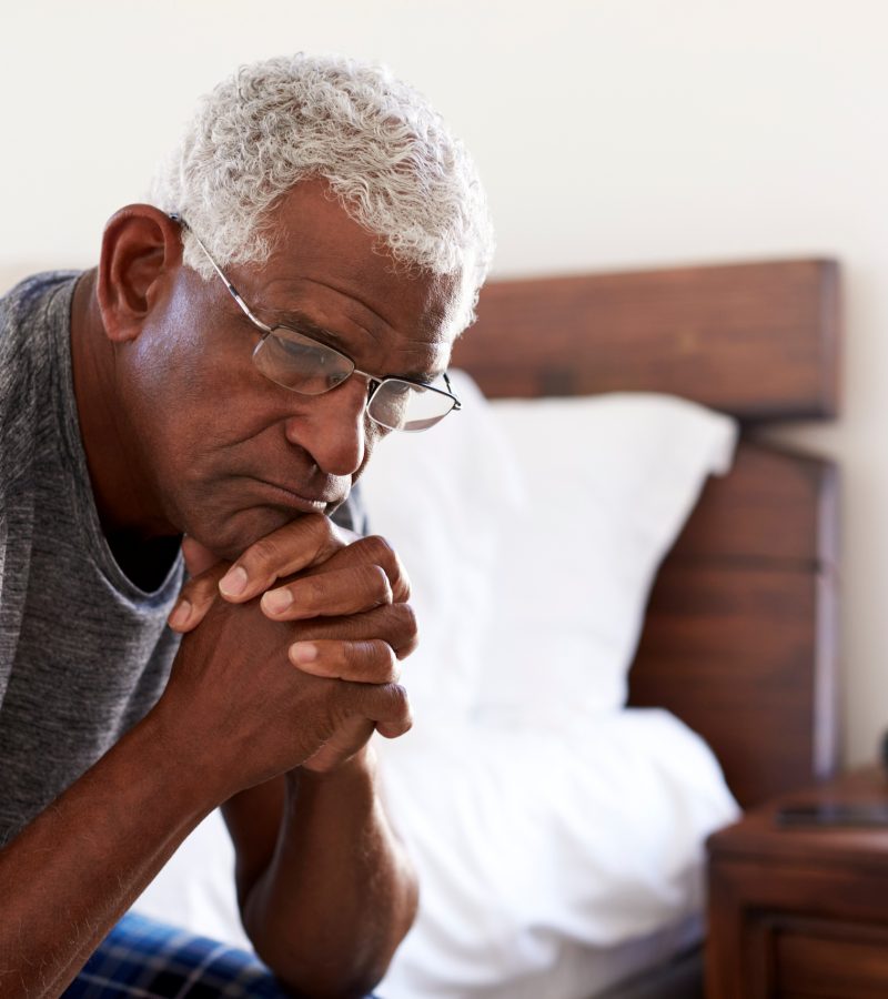 Solemn Senior Man Sitting On Side Of Bed At Home With Head In Hands